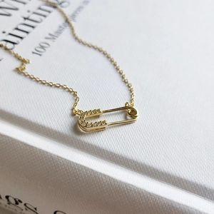Elegant gold safety pin pendant necklace with micro-pave crystals on white book background