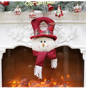 Close-up of a plush snowman Christmas ornament hanging by a warm fireplace with decor