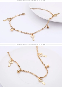 Close-up of gold anklet with key and ball charms featuring adjustable lobster clasp