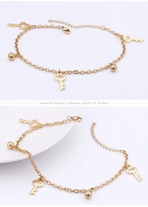 Detailed close-up of a gold key and bead charm anklet on a white ceramic plate