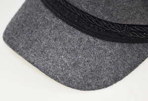 Close-up of wool octagonal cap with black braided strap and floral embroidery detail