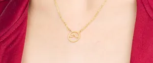 Close-up of golden wave pendant necklace worn by a model against a red background