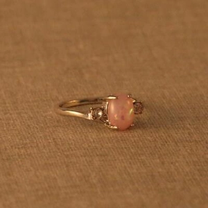 Nahaufnahme eines roségoldenen Rings mit ovalem rosa Opal und seitlichen Diamanten