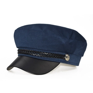 Detail of navy sailor cap showing textured fabric, black leather brim, and silver button decor