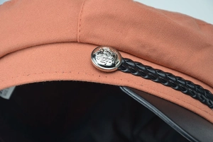 Detail of orange baker boy hat with black leather brim and silver crest button