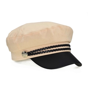 Detail of beige baker boy hat featuring a black faux leather brim and gold button