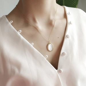 Close-up of oval white mother of pearl pendant with gold braided texture on a chain