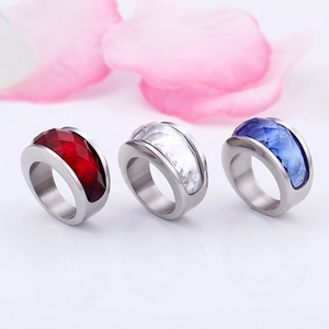 Polished stainless steel crystal rings in red, clear, and blue on white background
