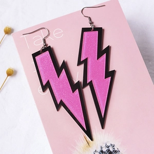 Macro shot of pink glitter lightning bolt earrings with silver hooks on a pink background