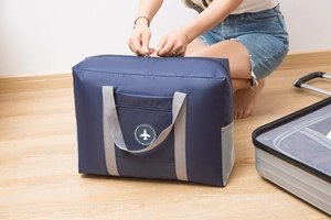 Detail of blue folding travel bag being packed next to a suitcase on wooden floor