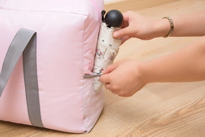 Close-up of pink travel bag showing side mesh pocket holding a folding umbrella