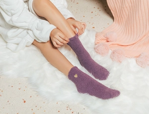 Detailed view of purple coral fleece socks with gold heart embroidery on a cozy rug