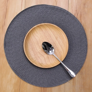 Detailed top view of dark gray woven placemat with wooden plate and steel spoon