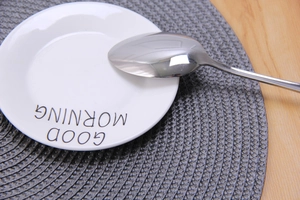 Close-up of ceramic plate with Good Morning text on grey woven round placemat
