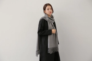 Detailed view of grey cashmere scarf with tassel edges worn over a black winter coat