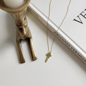 Detail of a minimalist gold key pendant necklace draped over an art book