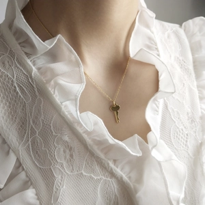 Close-up of a minimalist golden key pendant necklace worn on a white lace background