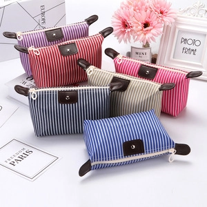 Stack of striped travel toiletry bags in purple, red, beige, and blue with leather pulls