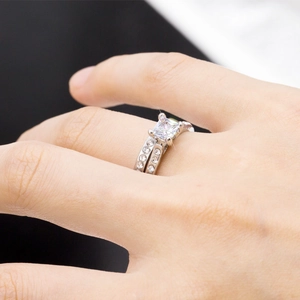 Close-up of a silver-tone bridal set with a square-cut main stone on a model's finger