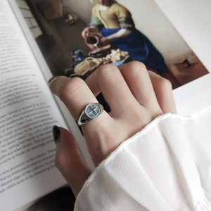 Detail of 925 sterling silver cross ring on finger with vintage artistic book background