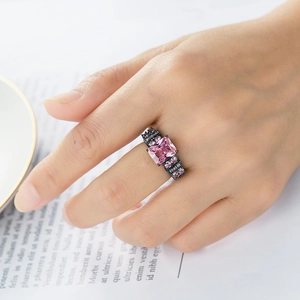 Close-up of pink square-cut zircon ring with black metal band on a magazine background
