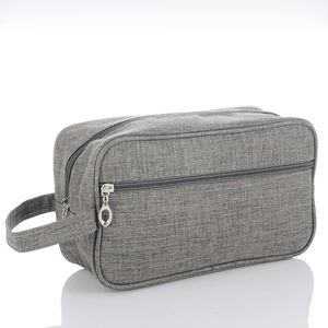 Detail view of a grey fabric toiletry bag with side handle and zipper pocket on white base