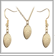 Detail of golden leaf jewelry set showing textured pendant surface and fishhook earrings