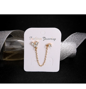 Detailed shot of golden chain drop earring with zircons on display card with ribbons