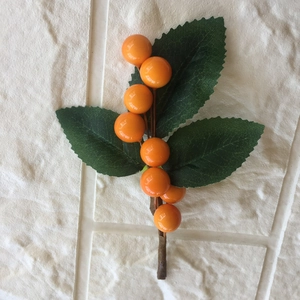 Artificial orange berry branch with green leaves on white textured background for home decor