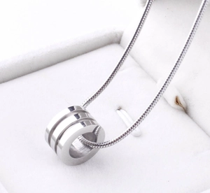 Macro shot of silver triple-ring pendant on snake chain inside white jewelry box