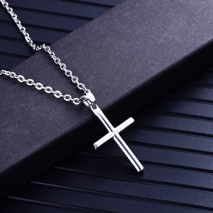 Polished silver stainless steel cylindrical cross pendant necklace on a dark textured box