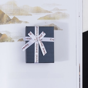Detail of navy blue textured jewelry gift box featuring a white satin ribbon with red text