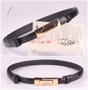 Detail of slim black patent leather belt with a minimalist golden rectangular buckle