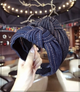 Close-up of blue denim wide headband with cross knot design and yellow contrast stitching