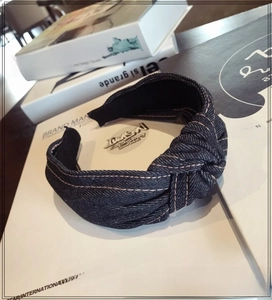 Close-up of deep blue denim wide headband with twisted knot and yellow stitching