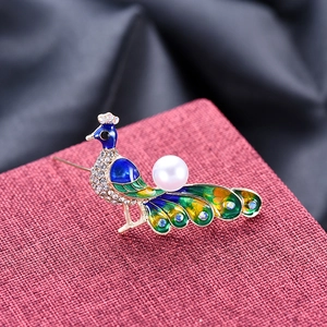 Luxury peacock brooch with colorful enamel feathers and pearl on a velvet box