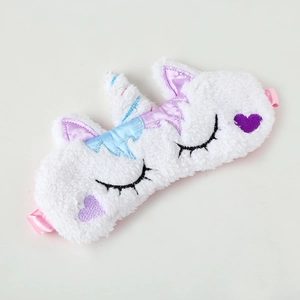 Close-up of white plush unicorn sleep mask with purple heart embroidery and pink ears