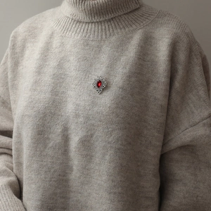 Retro vintage brooch with red teardrop gemstone on a grey knitted sweater