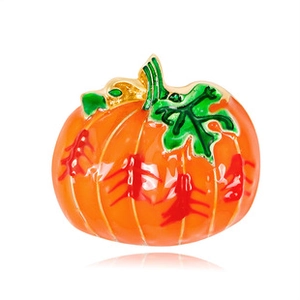 Detail view of a vintage pumpkin brooch with orange enamel finish and green metal leaf accents