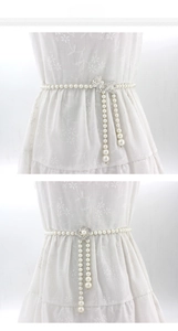 Détail d'une chaîne de taille en perles avec nœud en strass et boucle fleur sur robe blanche