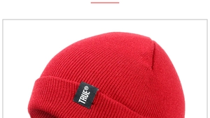 Close-up of red winter knit beanie showing fabric texture and TRUE logo tag detail