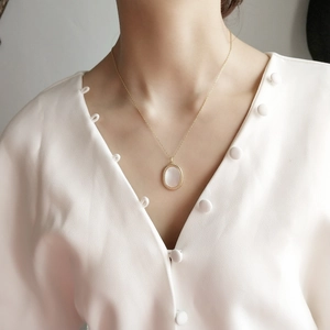 Close-up of gold oval shell pendant with woven texture on a white vintage cardigan