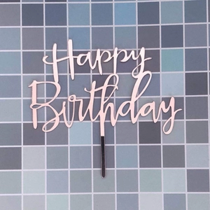 Pink Happy Birthday cake topper made of acrylic on a blue mosaic tile background