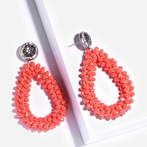 Detail van koraaloranje kralen oorbellen in druppelvorm met strass-steentjes op de knop