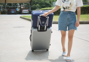 Detail of navy blue folding travel bag securely attached to a suitcase handle bar