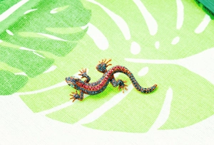 Detailed close-up of a lizard brooch featuring blue and pink crystals on a leaf pattern