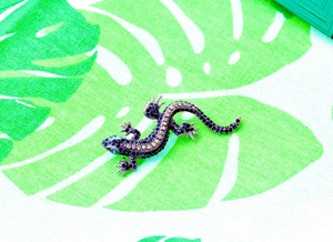 Detail of gecko brooch featuring dark rhinestones and green crystal eye on fabric