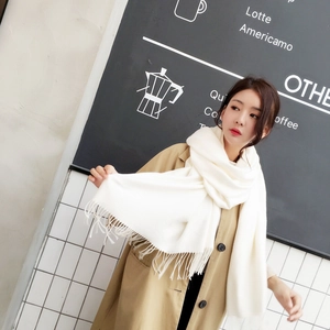 Detail of a thick cream knit cashmere scarf with long tassels on a beige wool coat