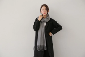 Detail of grey cashmere-feel scarf featuring soft tassels paired with a black wool coat