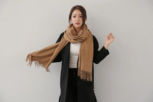 Detail of soft camel cashmere-like winter scarf with elegant fringe trim on a black coat